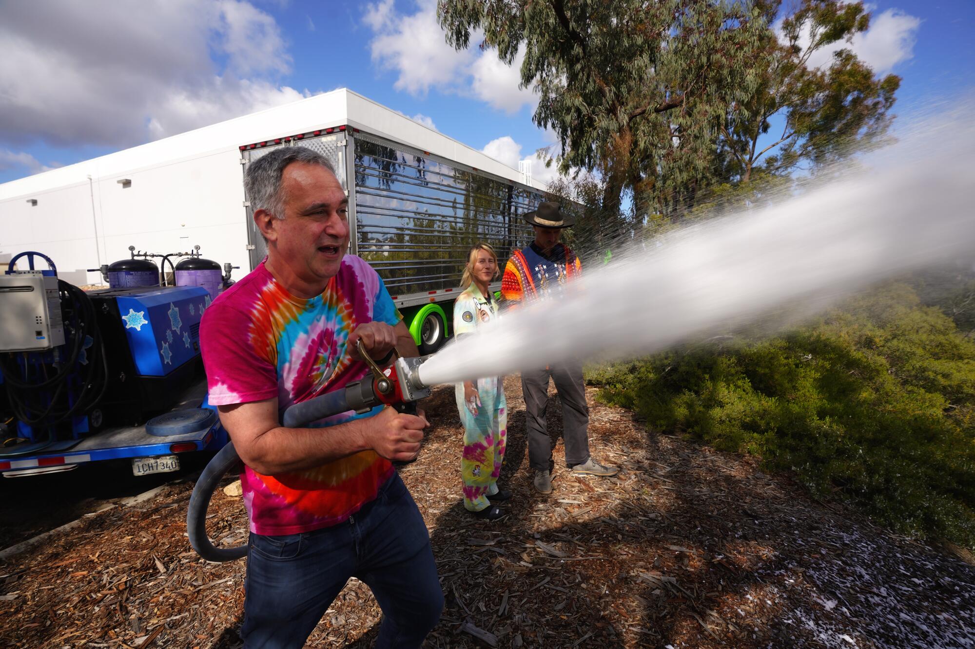 A man spraying white foam from a hose outside a building as others watch