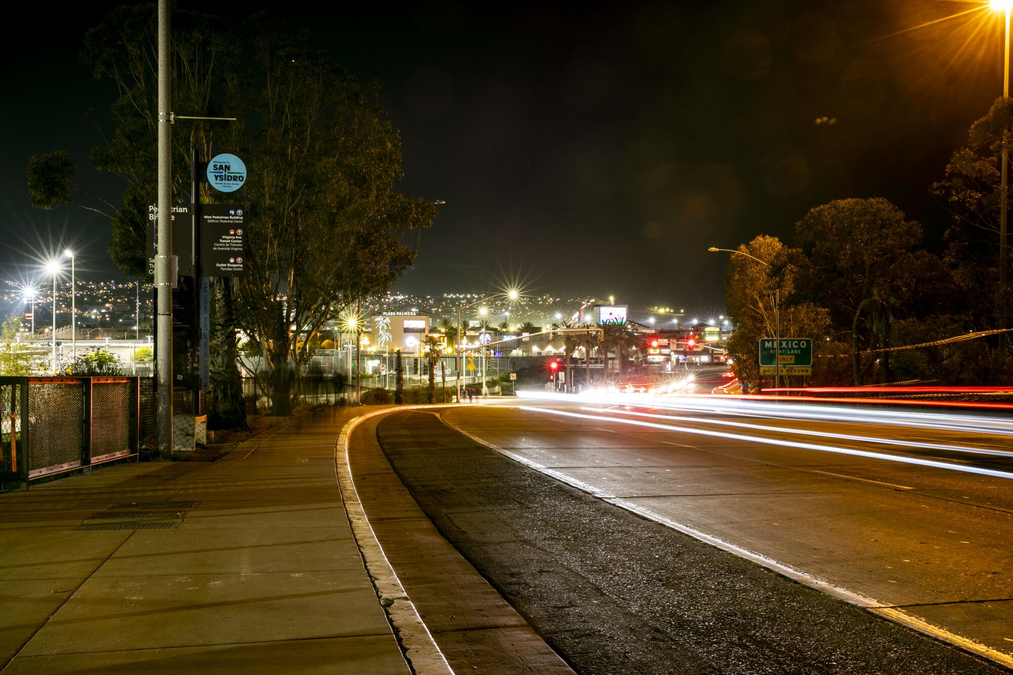 With the hills of Tijuana, Mexico, illuminated in the background, cars speed by along Camino de la Plaza 