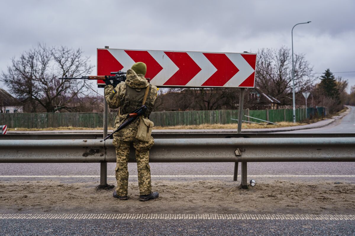 A soldier stands alongside a highway holding up a rifle.