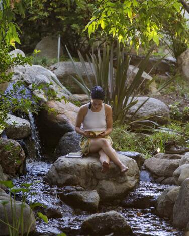 A woman reads next to a waterfall. 