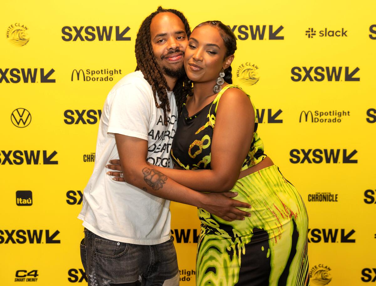 A man and a woman embrace in front of a South by Southwest backdrop