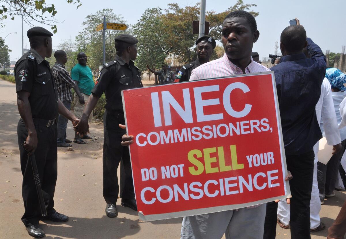 People hold signs to protest the postponement of Nigeria's election as police officers hold hands to block protesters in the capital city of Abuja on Saturday. The delay was called by the Independent National Electoral Commission, or INEC.