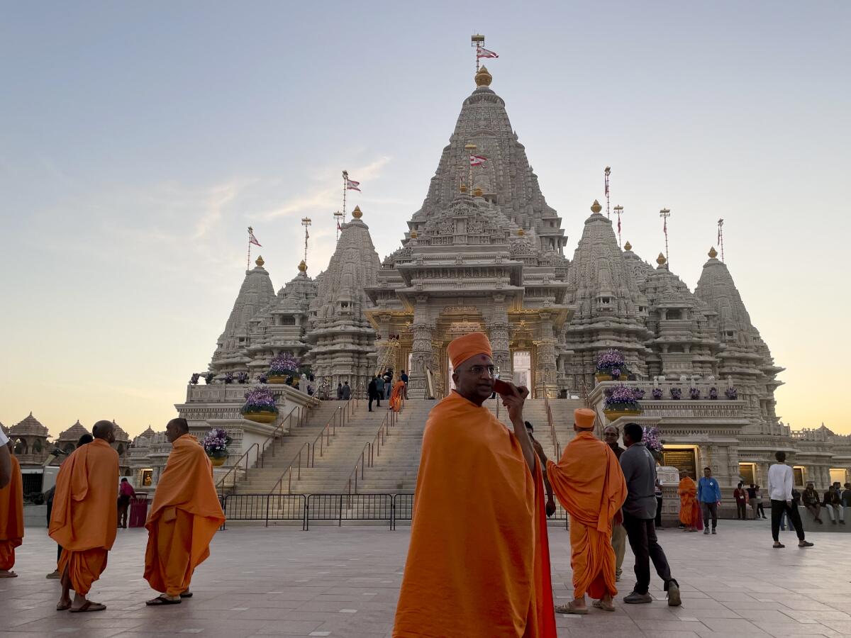 Monks in saffron robes walk in front of a Hindu temple.