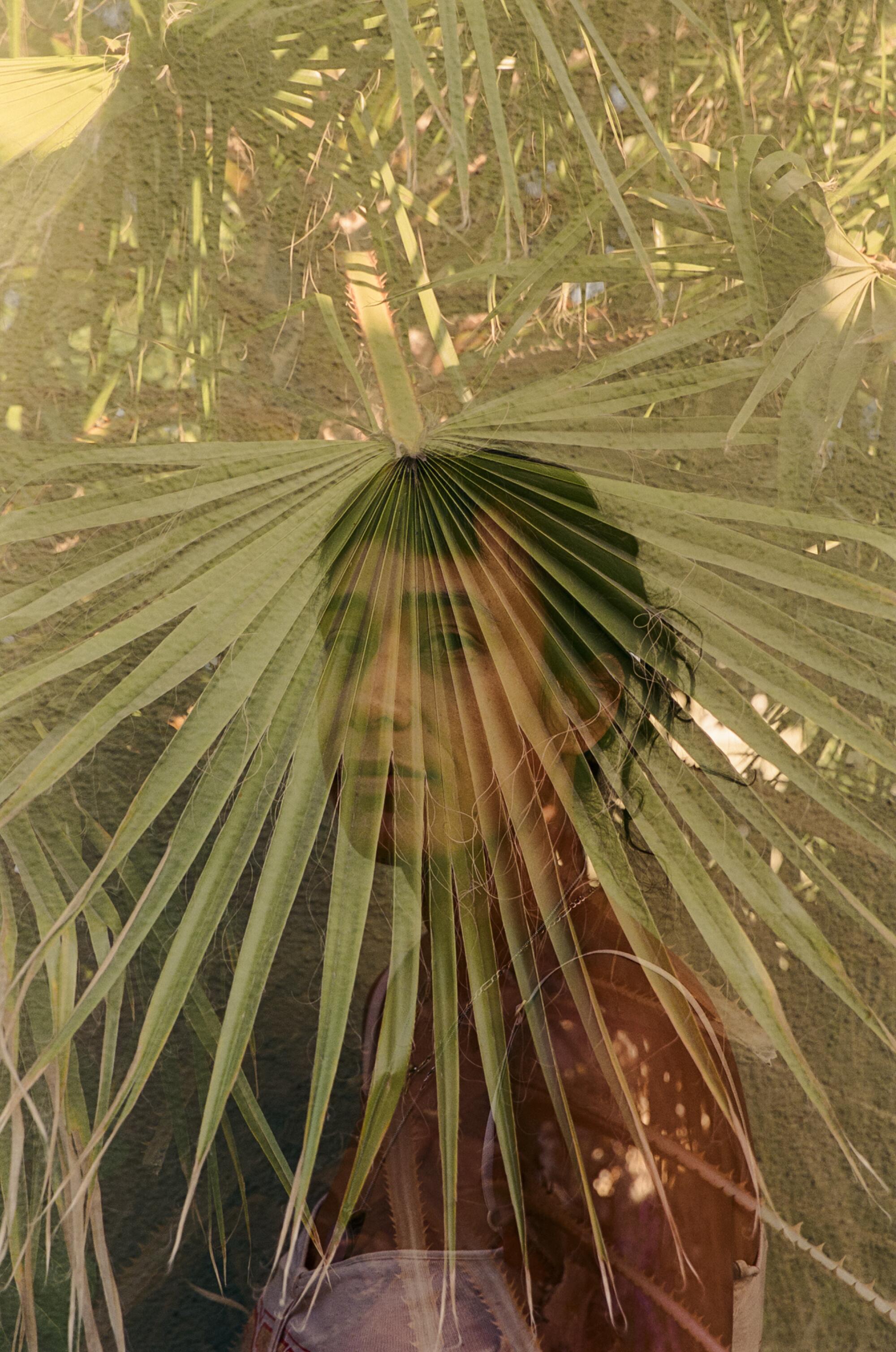 An artist in profile poses with a palm superimposed over her face. 