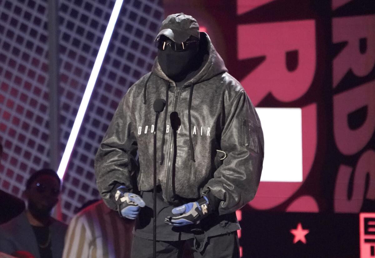 A person covered head to toe in black, wearing a hat, gloves, jacket, face mask and dark glasses