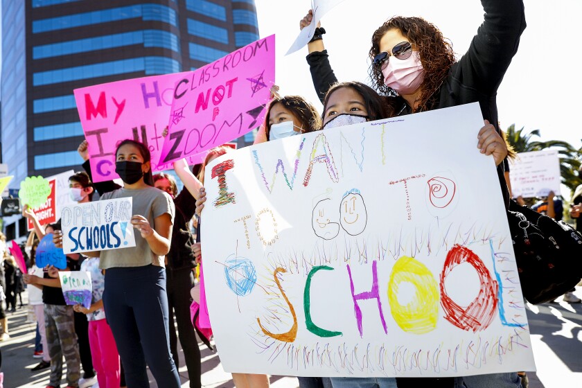 Parents and students participate in a protest with signs calling on LAUSD to reopen classrooms.