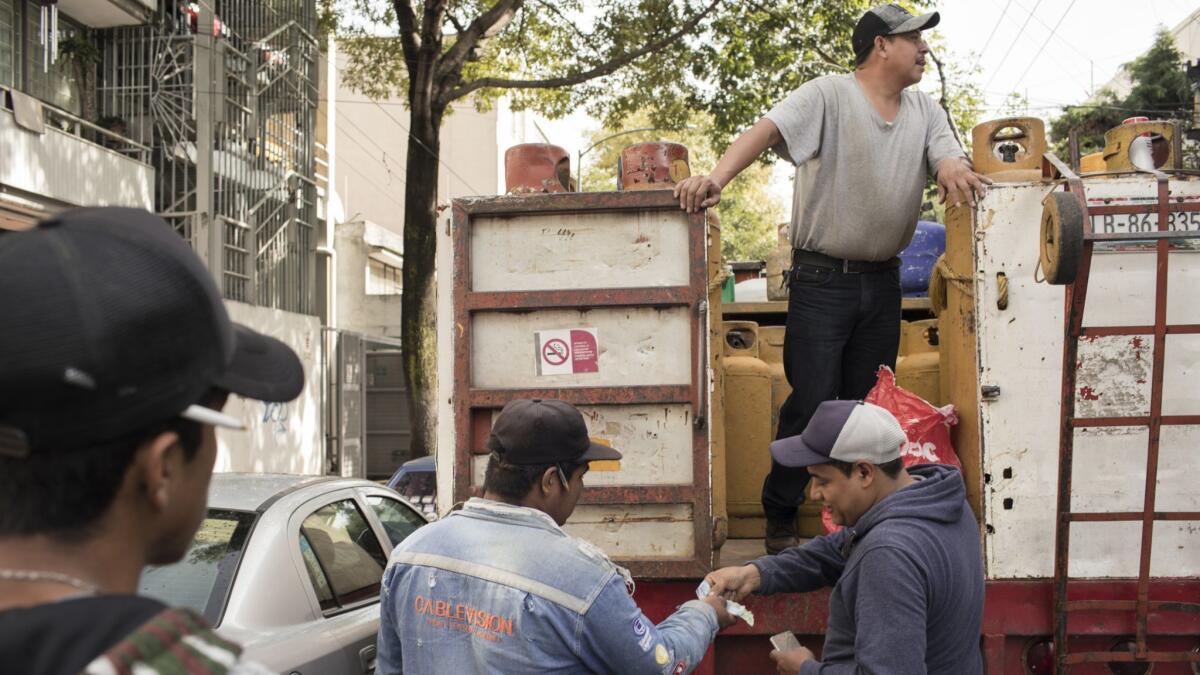A customer pays Jorge Alberto Rodriguez, center, for a gas canister while Agustin Martinez looks for potential buyers from his perch on their gas delivery truck in Mexico City.