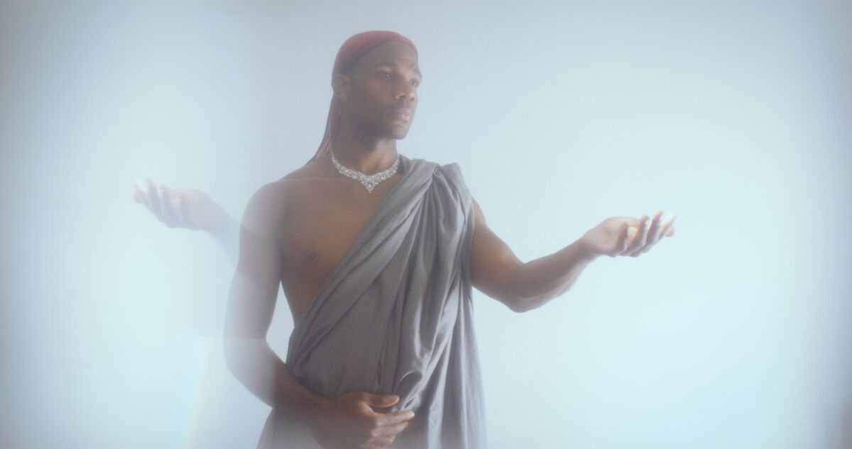 A foggy image shows a performer in a do-rag and a toga-like garment