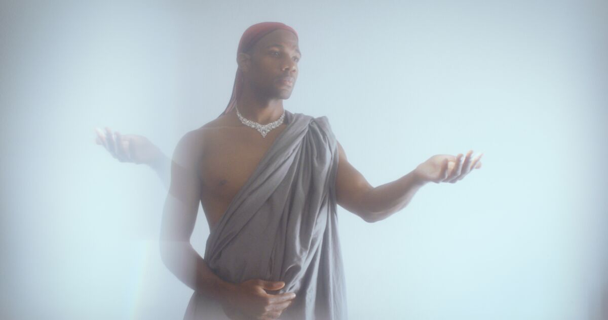 Wearing a diamond necklace and red durag, Derrell Acon performs "Songs to the Dark Virgin."