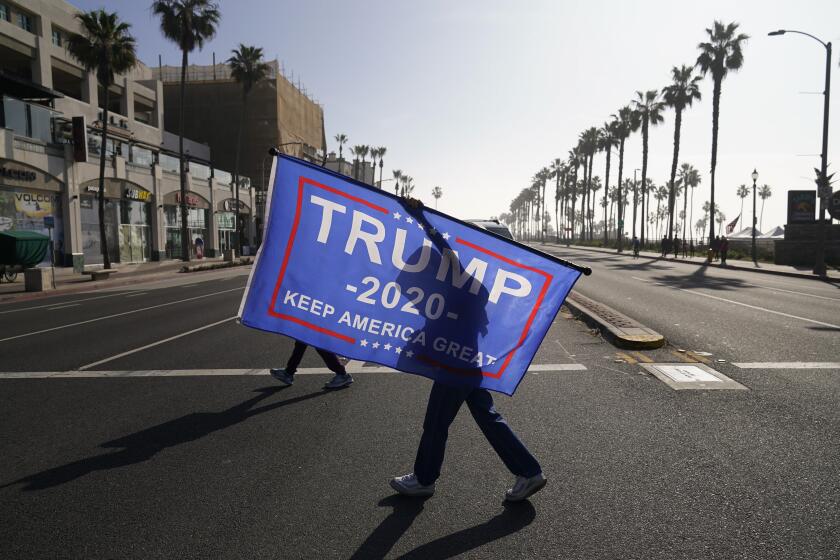 FILE - A woman walks across the street with a flag supporting President Donald Trump during a rally Jan. 6, 2021, in Huntington Beach, Calif. A state GOP rule change has opened the possibility that former President Donald Trump could sweep California’s entire trove of delegates in the March 5 primary, the plumpest prize in the party’s nominating contest. The election falls on Super Tuesday, when California is among more than a dozen states holding primaries and the largest number of delegates are up for grabs of any single day. (AP Photo/Jae C. Hong, File)