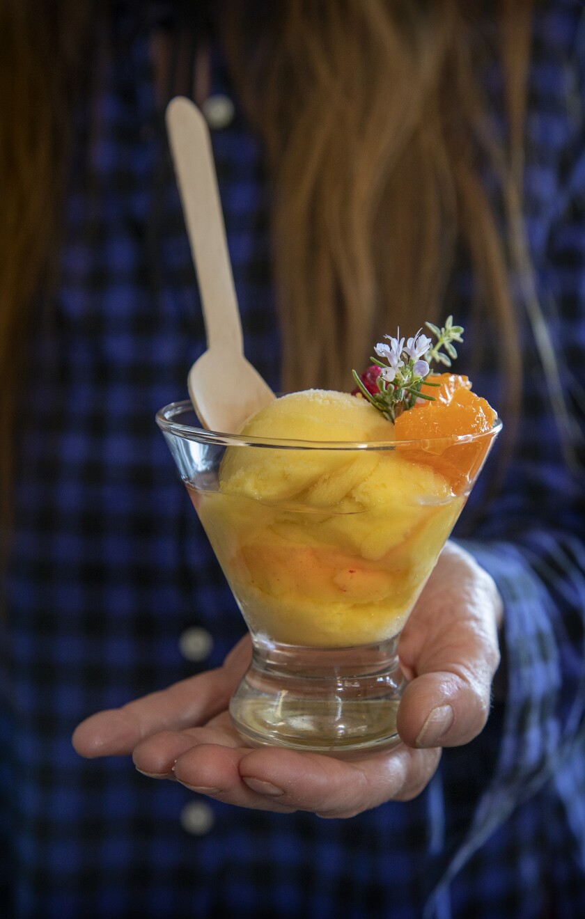 A hand holds a  yellow and orange sorbet cocktail