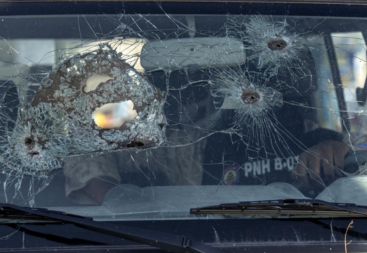 A police officer sits inside his vehicle with a windshield damaged by bullet holes