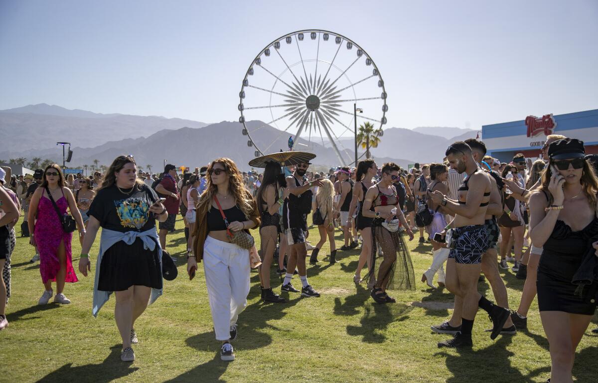 Hundreds of festivalgoers walk on grass in front of a Ferris wheel at Coachella