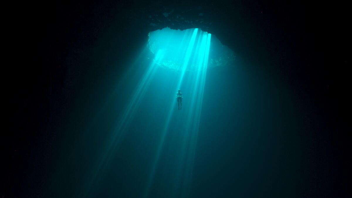 A freediver framed in blue light shining through a blue hole