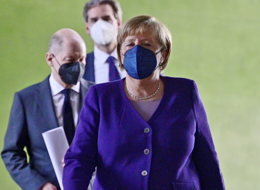 La canciller alemana Angela Merkel, seguida por el ministro de finanzas Olaf Scholz, izquierda, arriba a una conferencia de prensa tras una reunión con los jefes de gobierno de los estados federales el 2 de diciembre del 2021 en Berlín. (John Macdougall/Pool Foto via AP)