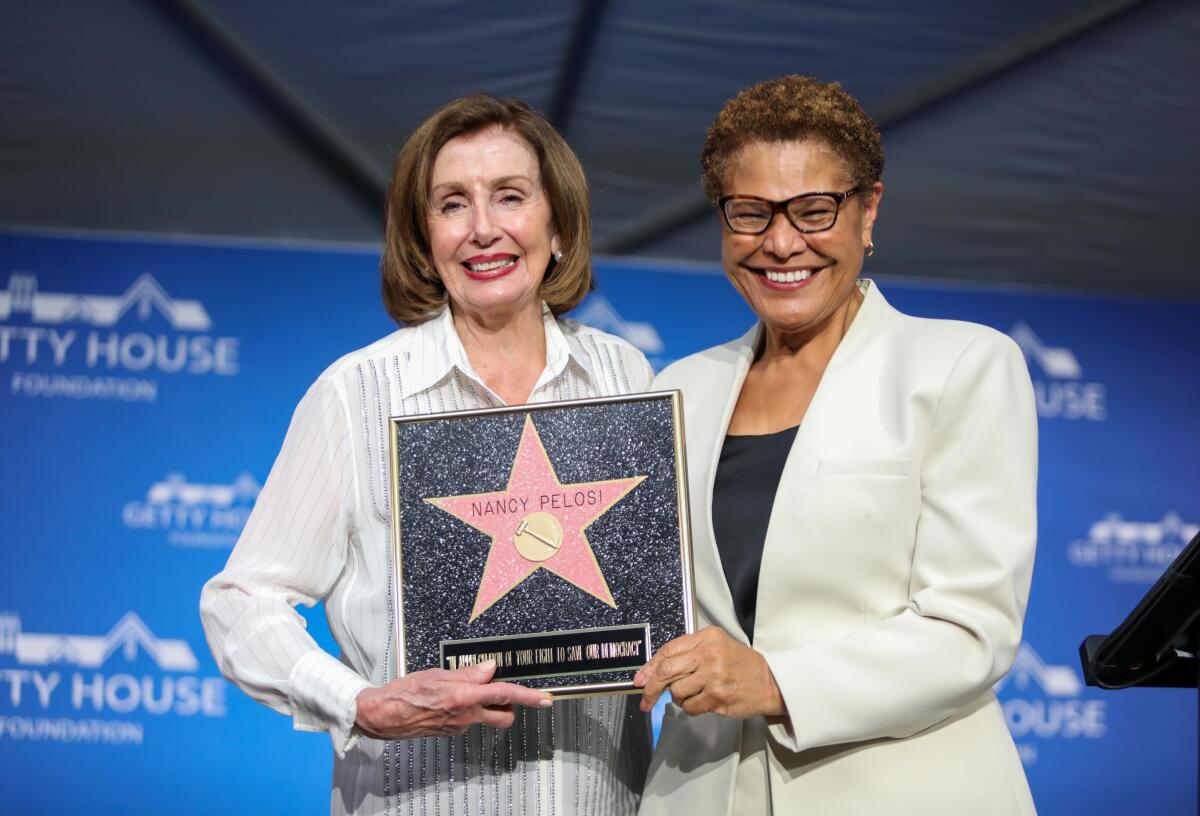 Bass and Pelosi smiling holding a plaque