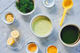 An overhead photo of aioli components on white marble: bowls of dill oil, vinegar, a bunch of fresh dill and a citrus juicer