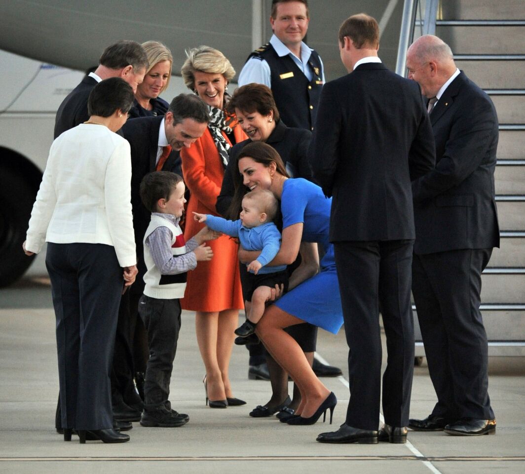 Lorraine and Ian Watts, left, Chief Minister Katy Gallagher, Minister Andrew Leigh, Foreign Minister Julie Bishop (orange), Lynne Cosgrove, Britain's Prince William and Governor General Peter Cosgrove watch as Theodore Leigh plays with Prince George held by Catherine, Duchess of Cambridge, after they arrived at Defence Establishment Fairbairn in Canberra on April 20, 2014.