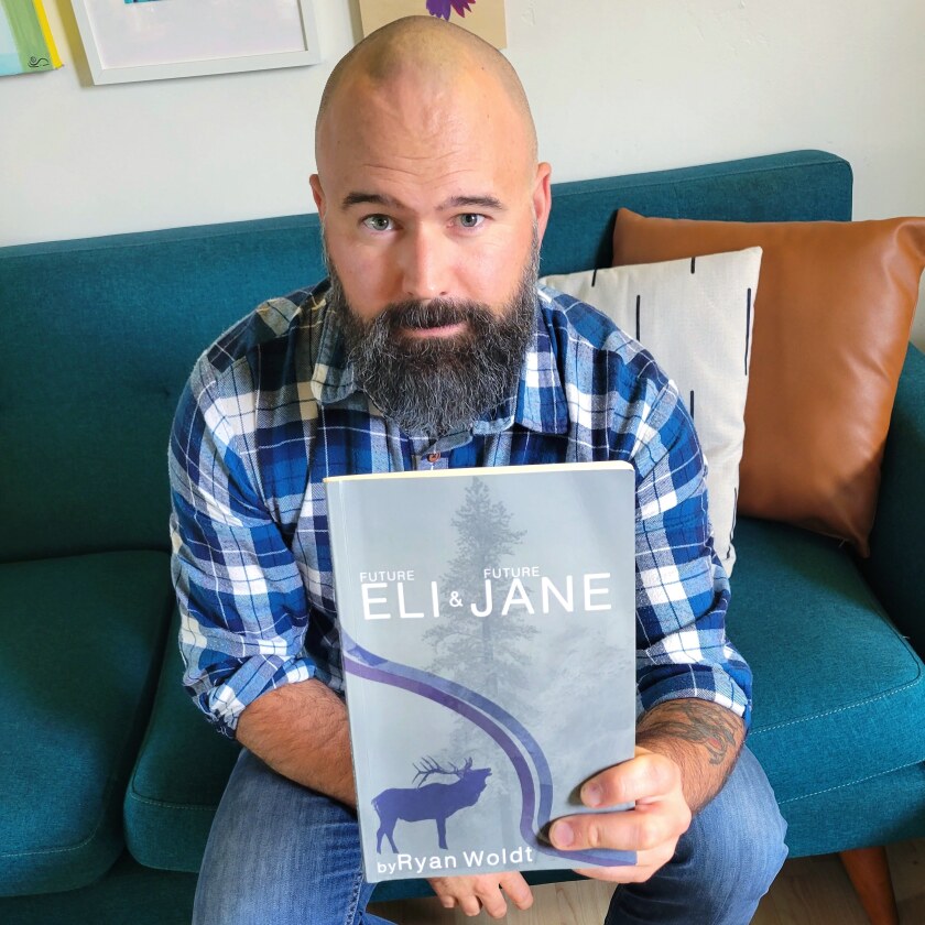 A bearded man sitting on the couch holding a book