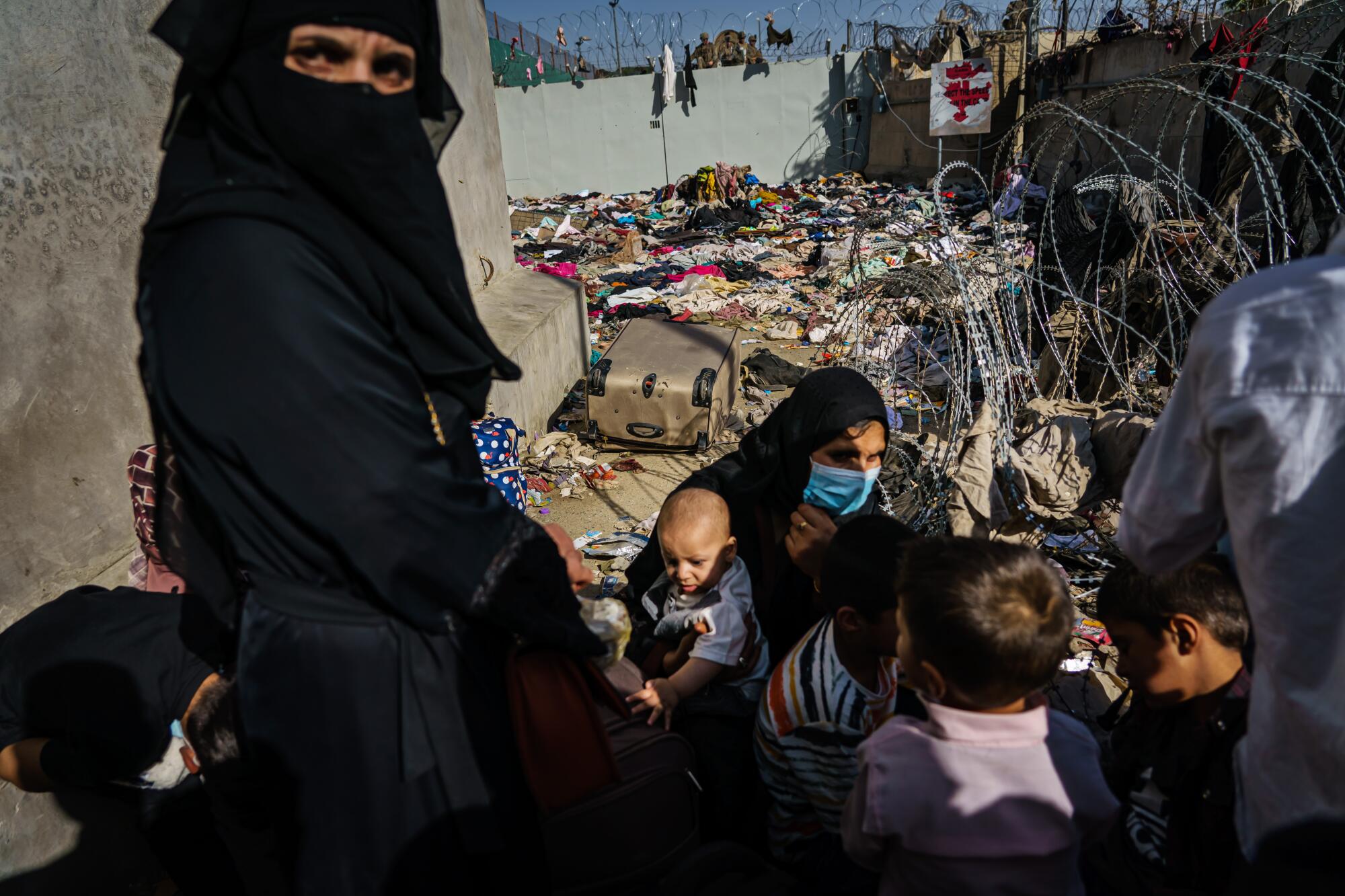 A woman in a black burqa next to women and children crouching near barbed wire