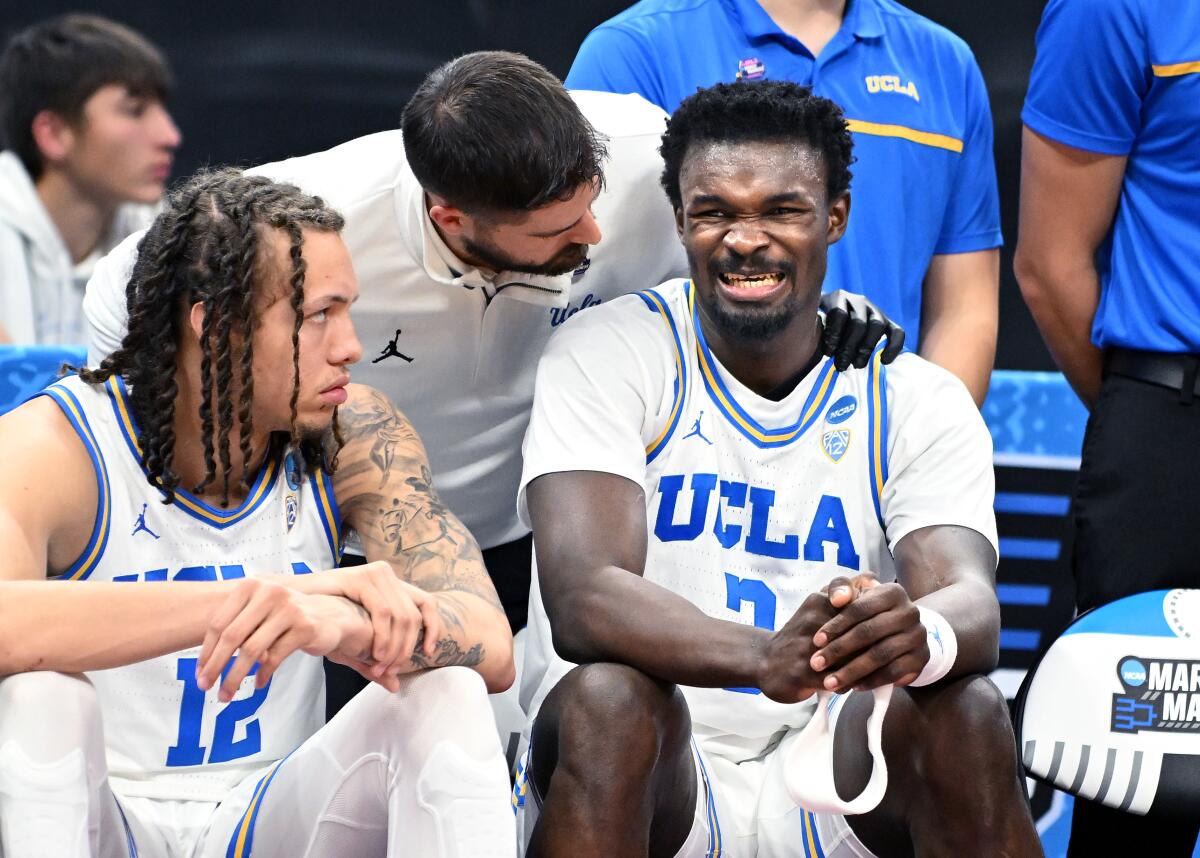 UCLA's Adem Bona grimaces in pain after coming out of the game against Northwestern as teammate Mac Etienne looks on.