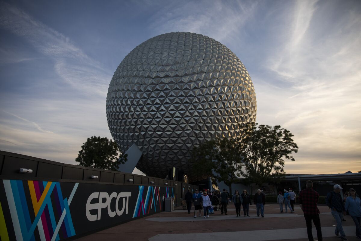 A golf-ball-like structure near a wall with the word EPCOT and people standing in front 