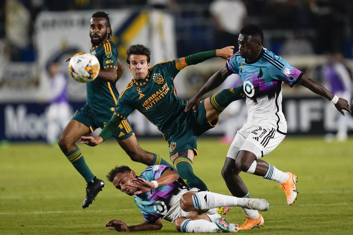 Galaxy midfielder Riqui Puig shoots over Minnesota United midfielder Hassani Dotson and forward Bongokuhle Hlongwane.