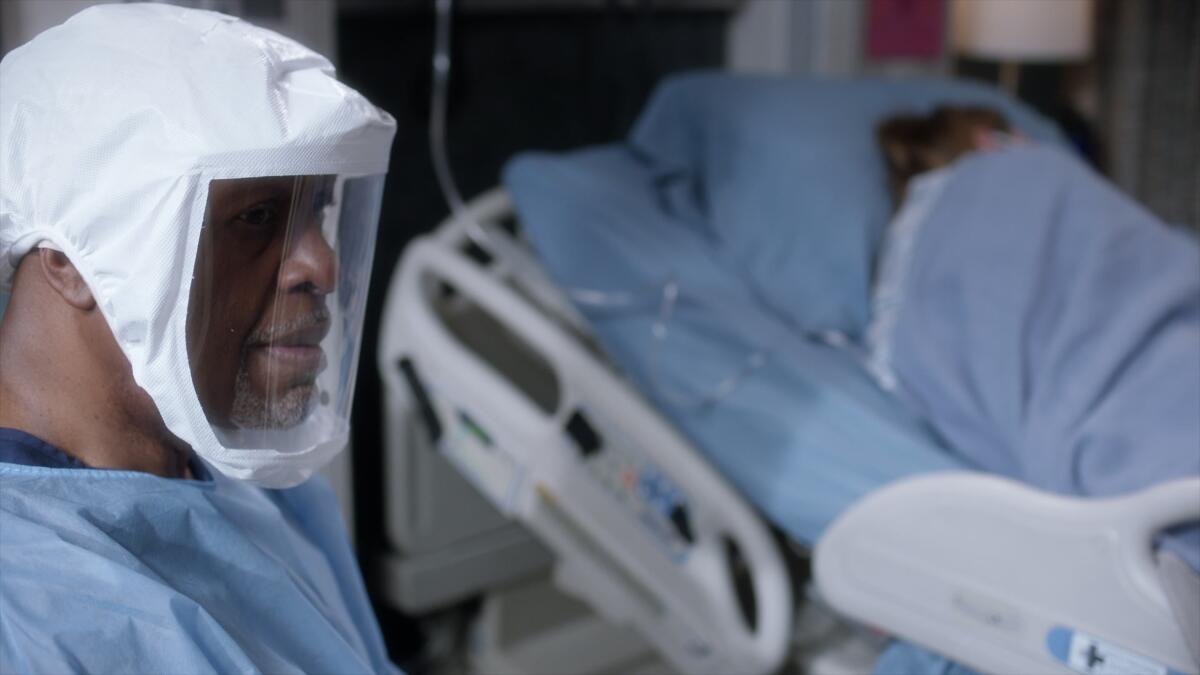 A man in full PPE sits at a hospital patient's bedside in "Grey's Anatomy."