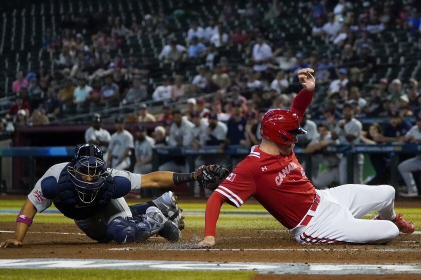 Canada's Freddie Freeman, right, scores on a throwing error from Great Britain first baseman Nick Ward (not shown) to catcher Harry Ford, left, during the first inning of a World Baseball Classic game in Phoenix, Sunday, March 12, 2023. (AP Photo/Godofredo A. Vásquez)