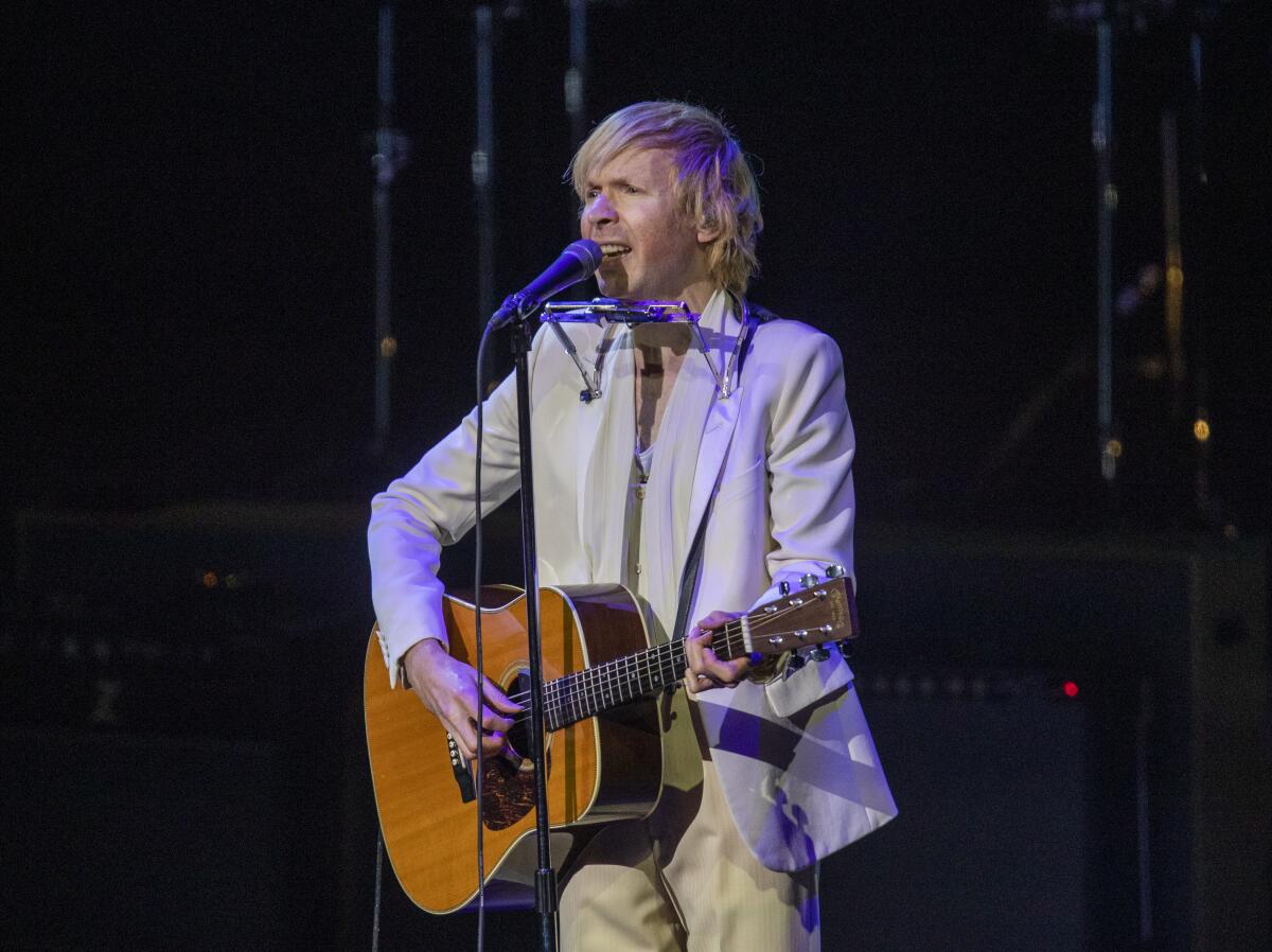 Beck plays his guitar and sings into a microphone. 