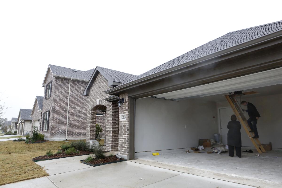 Two people work on the garage of a large single-family home in suburban McKinley, Texas.