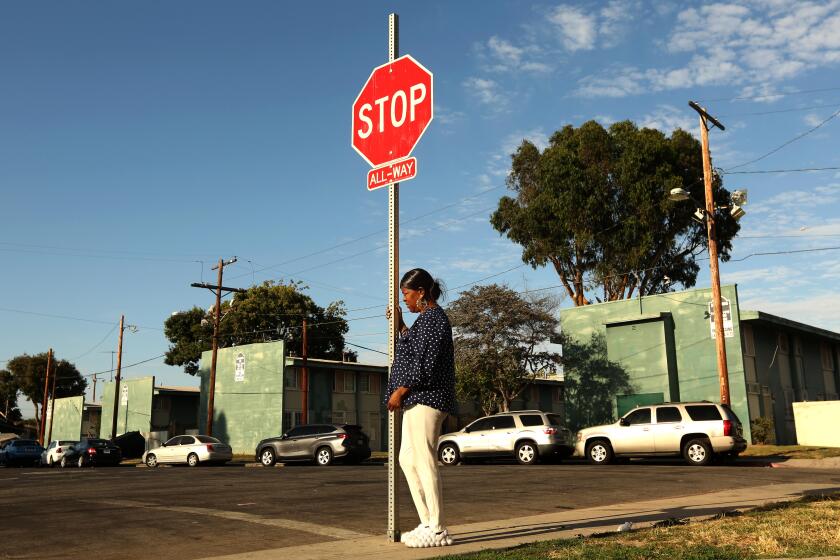 WATTS, CA - AUGUST 1, 2023 - Dr. Cynthia "Big Mama" Mendenhall waits for a friend under a symbolic sign with her wishes for gun violence to end at the Imperial Courts housing project in Watts on August 1, 2023. Dr. Mendenhall was waiting for a friend to meet her at the spot. She lost two sons to gun violence in 2006 and continues to live in Imperial Courts. Watts has been the site of violence in recent weeks with multiple people dying and 9 people being shot in Imperial Courts and Jordan Downs housing projects. (Genaro Molina / Los Angeles Times)