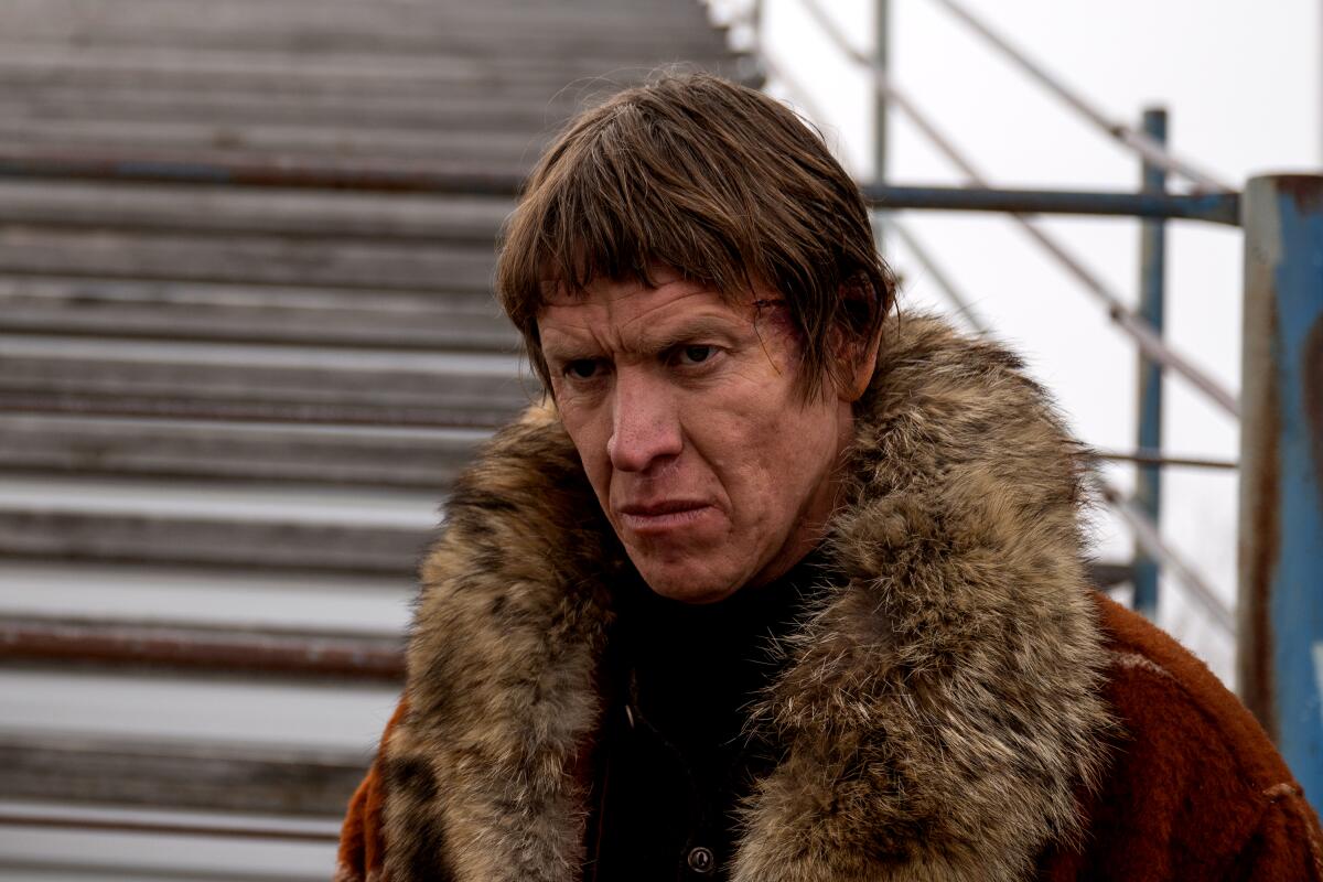 Um homem com um corte de cabelo largo usa um casaco com gola de pele do lado de fora, "Fargo."