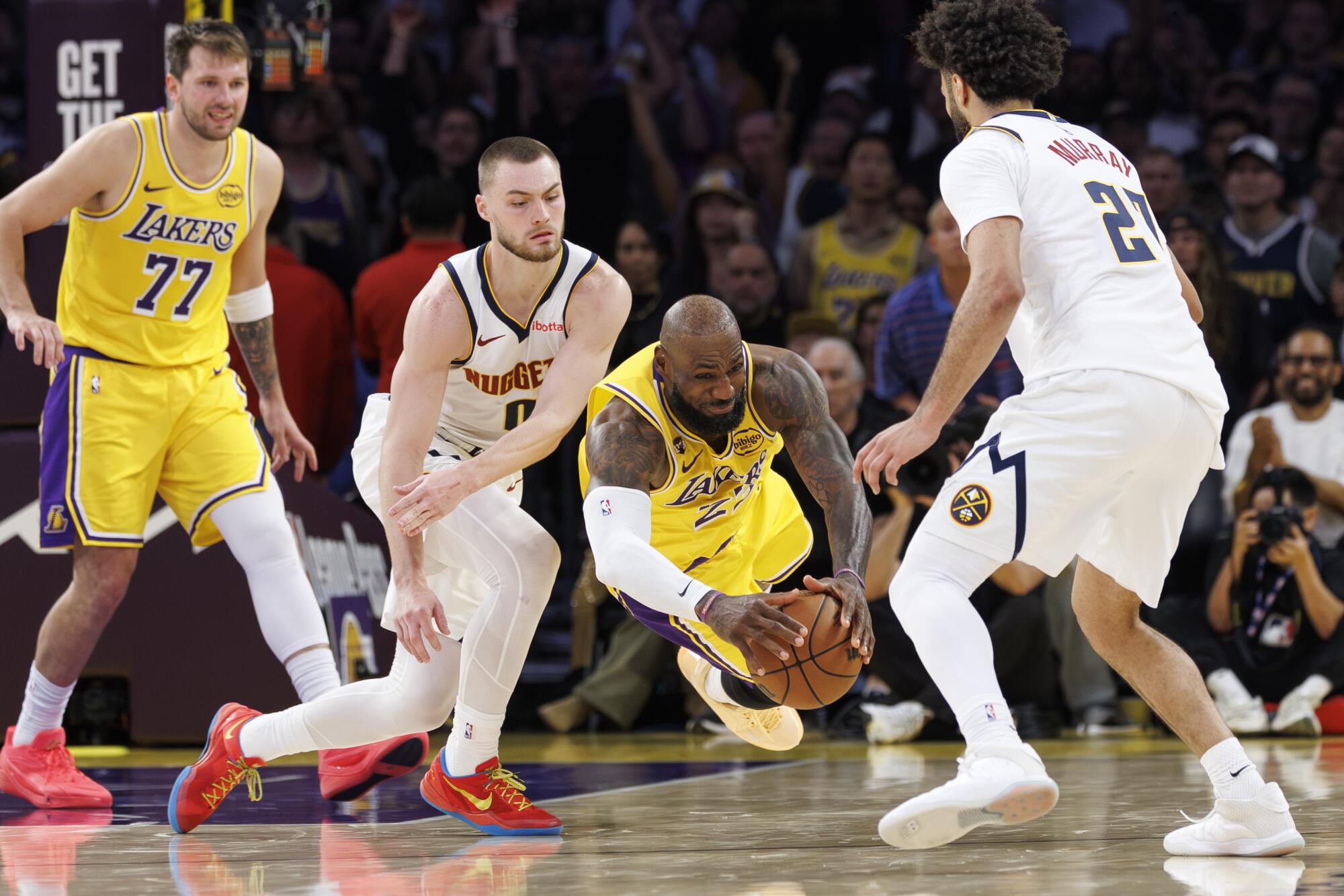 Lakers'ın yıldızı LeBron James, Denver Nuggets'ın guardları Christian Braun (0) ve Jamal Murray arasında topa atlıyor.