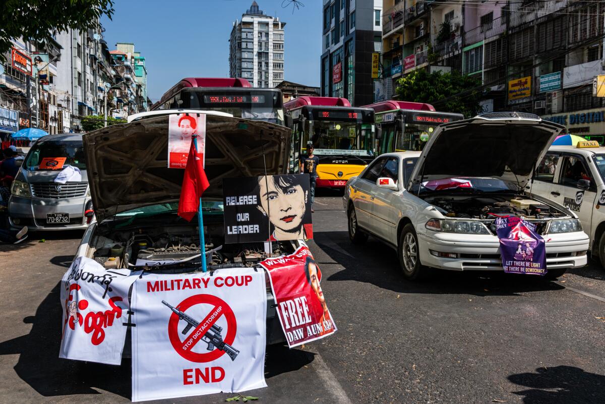 Taxis with hoods open and bearing signs sit on a road in Yangon, Myanmar. 