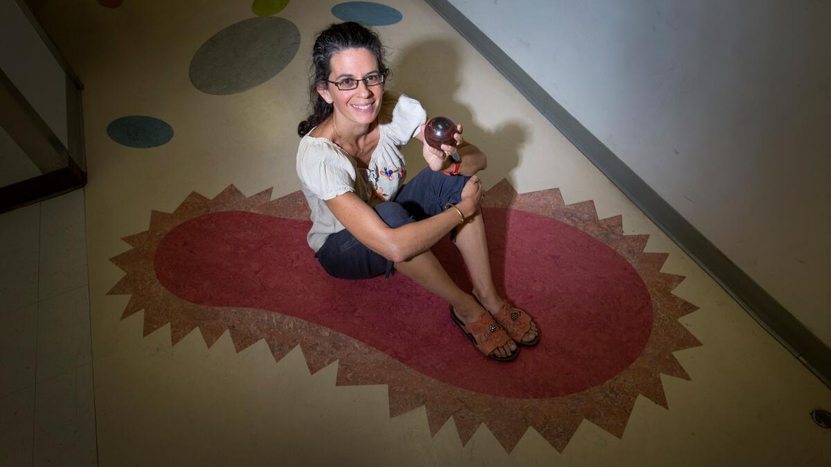 Microbiologist and new MacArthur fellow Dianne Newman sits on a linoleum microbe outside her office at Caltech. That's a 2-billion-year-old rock in her hand.