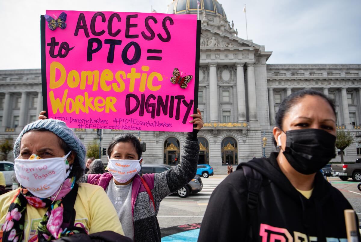 Women stand in front of City Hall, one with a sign promoting domestic workers' rights