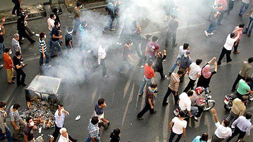 Protesters march around a smoldering trash bin on a street in central Tehran.