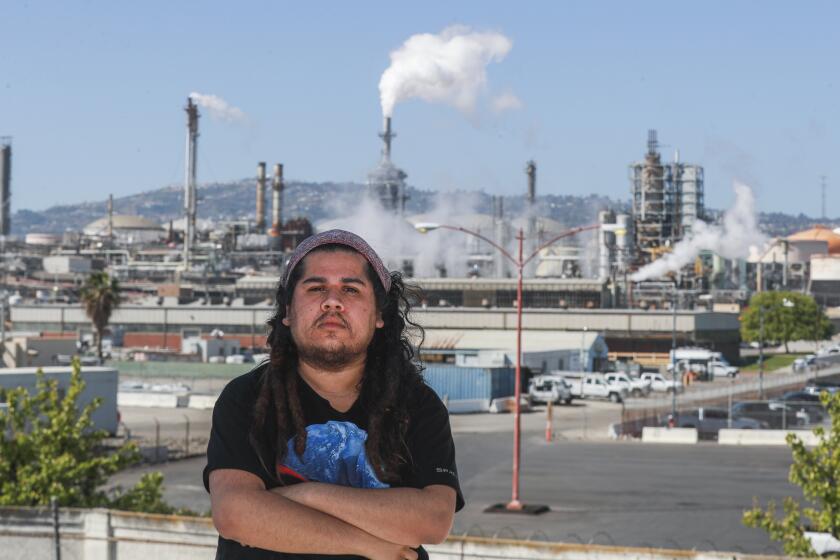 Wilmington, CA - March 14: Ulises Flores, 23, was born and raised in Wilmington, shown on the roof of his home which hugs the fence line of the Phillips 66 refinery complex in Wilmington. Since the age of 13, Ulises has suffered from breathing problems due to swelling in his sinuses and nostrils, at times leaving him with headaches. Doctors told him it was likely due to air pollution. He is one of many in his neighborhood who experience health problems tied to pollution. Photo taken Monday, March 14, 2022 in Wilmington, CA. (Allen J. Schaben / Los Angeles Times)