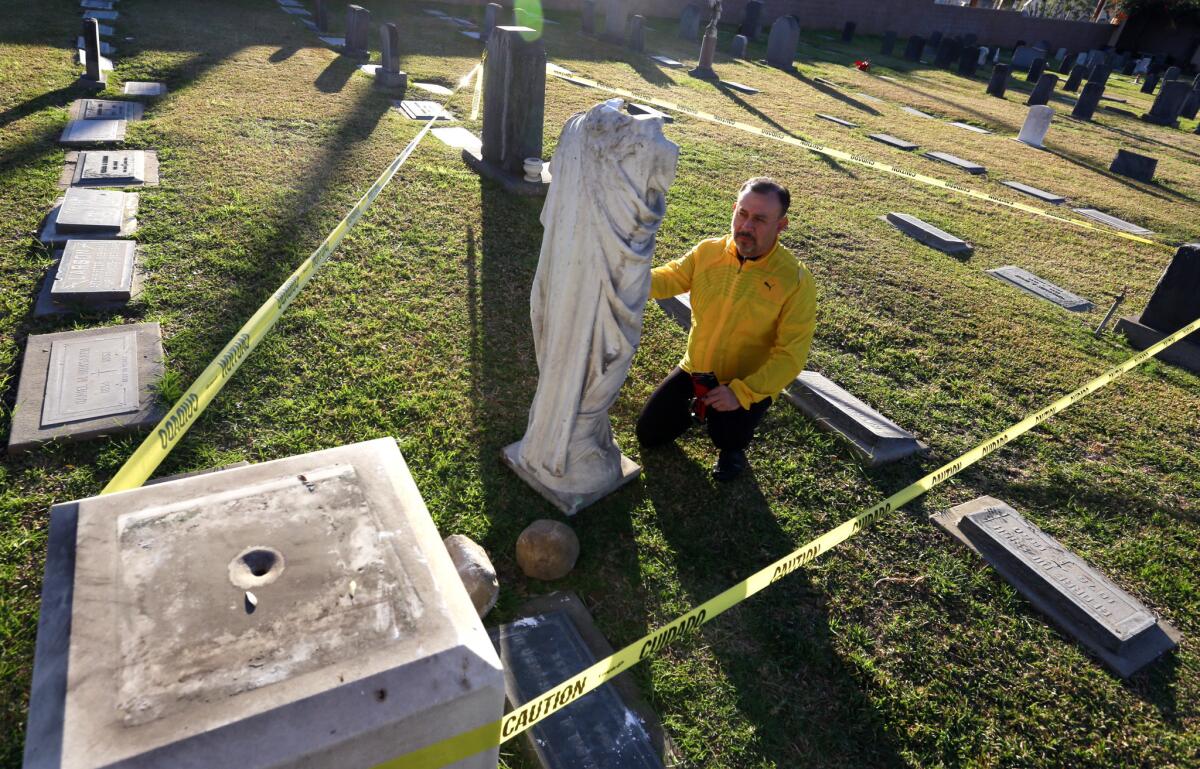 Father Tony Diaz kneels beside a statue of Jesus damaged by vandals this week at the San Gabriel Mission Church Cemetery.