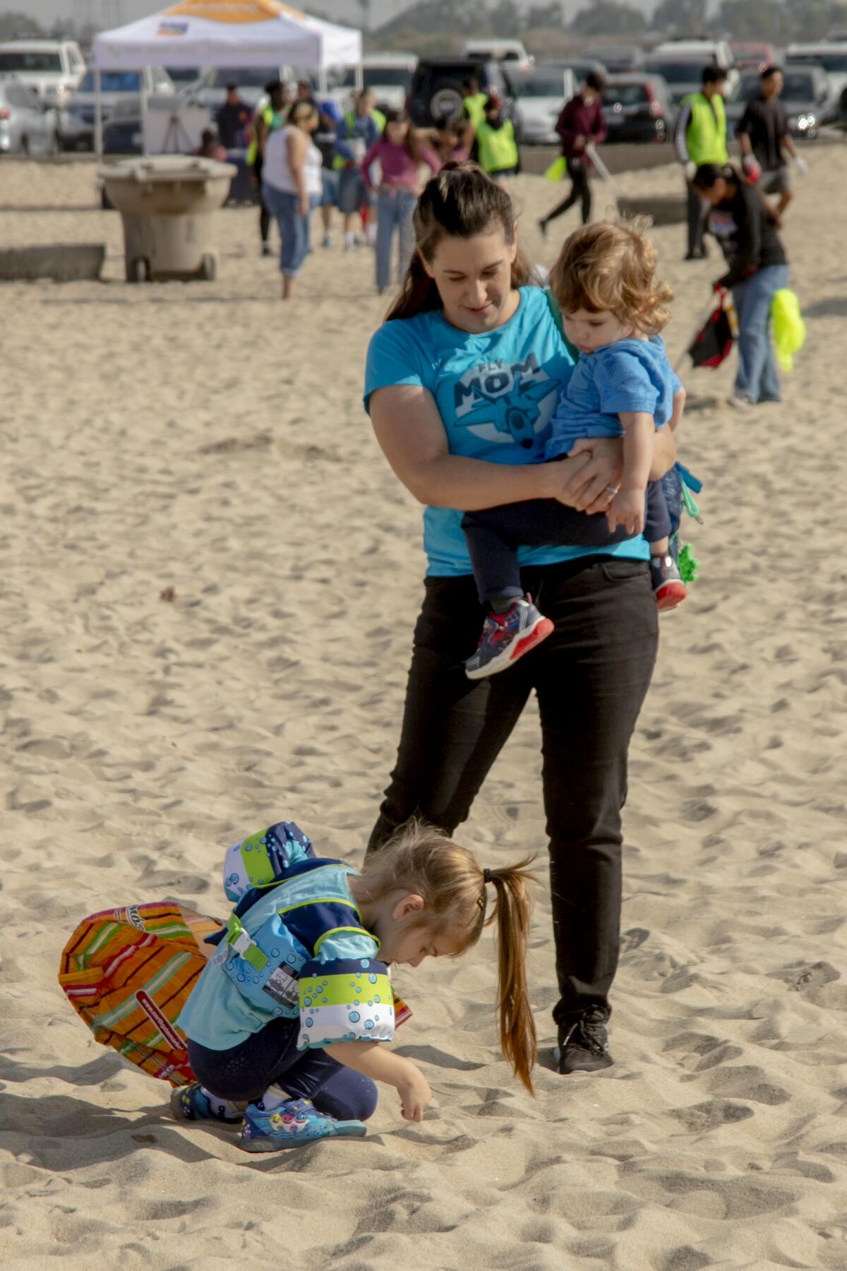 As mom Shannon Champ holds 20-month-old Thomas, as daughter Daphnie searches the sands for refuse.