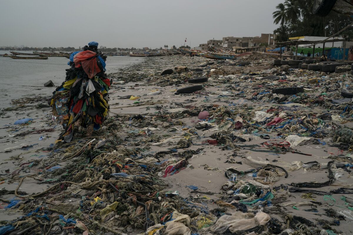 The environmental activist Modou Fall walks on a beach littered by trash and plastics.