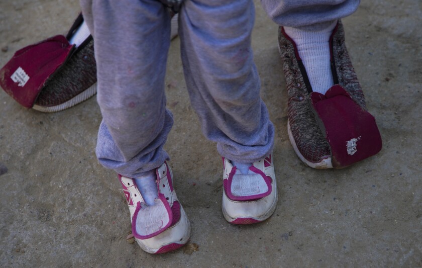 An adult and child seeking asylum arrive at a Tijuana migrant shelter without shoe laces