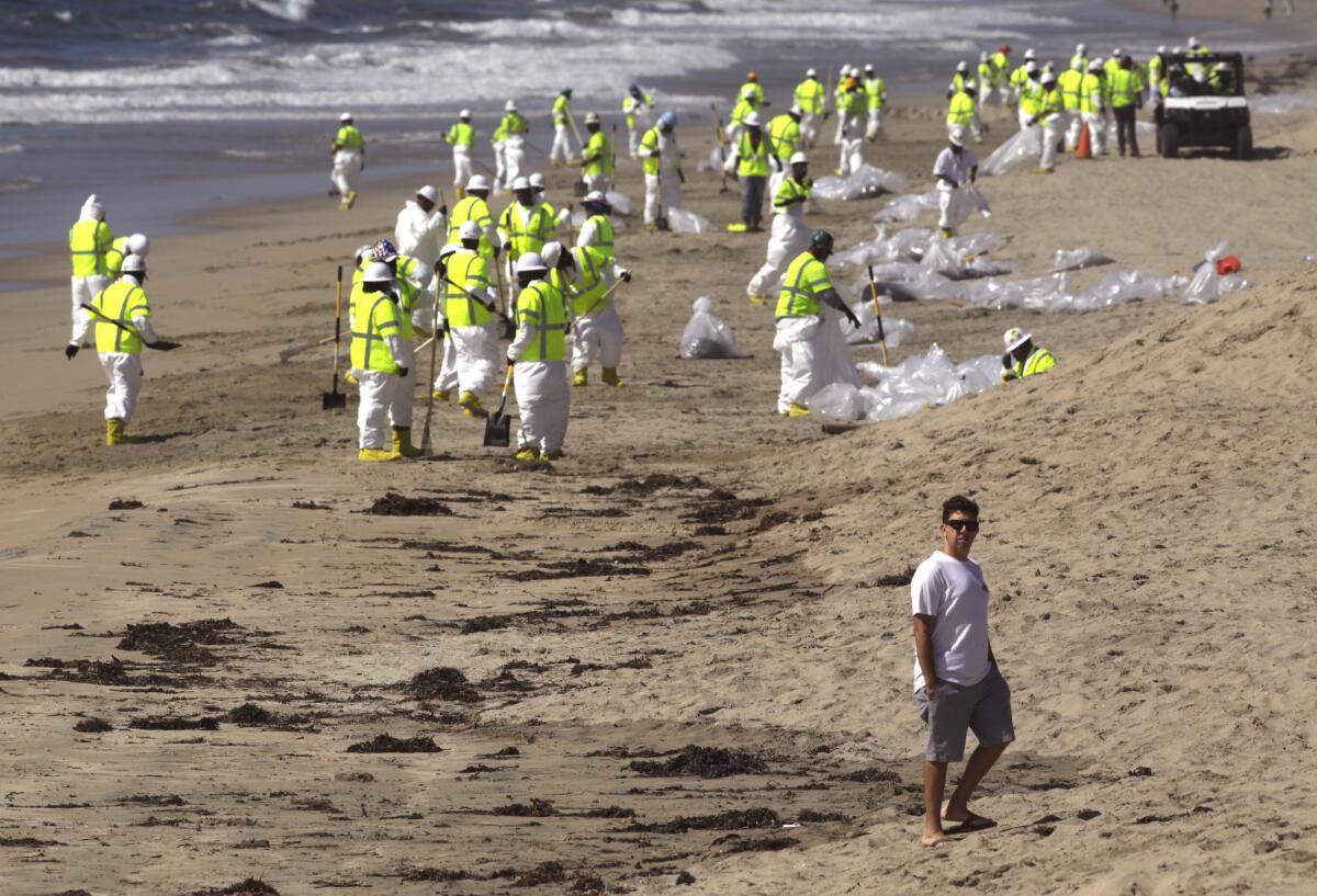A beachcomber walks past workers cleaning the beach