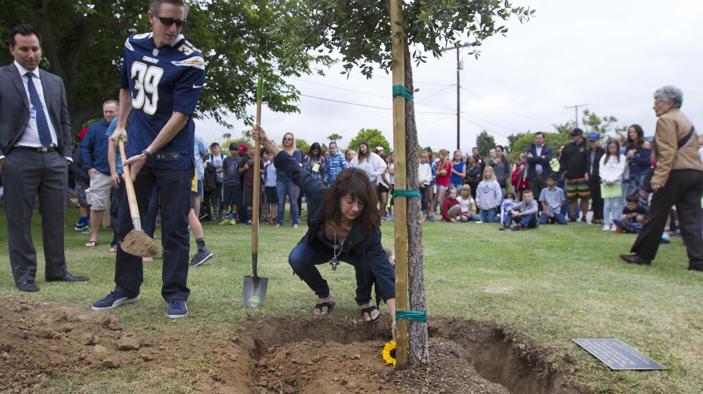 Murphy McCann, left, looks on as his wife, Bernadette, lays a flower in front of a memorial tree in honor of their son Brock during a special event at Newport Heights Elementary School in Newport Beach on Thursday. Third-grader Brock McCann was hit and killed by a trash truck while riding his bike home from school one year ago.