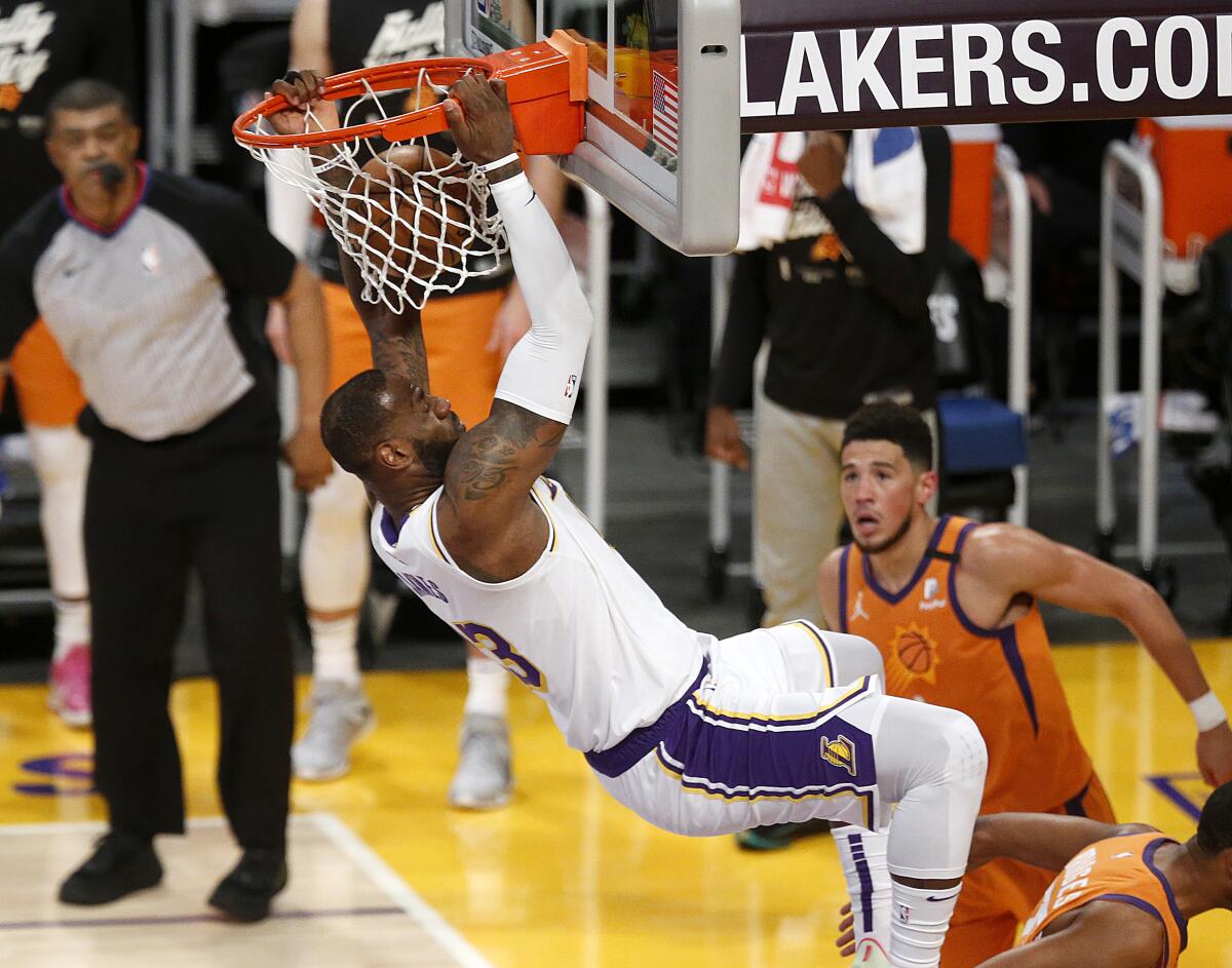 Lakers forward LeBron James hangs on the rim after throwing down a dunk off an alley-oop from Alex Caruso.