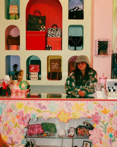 A woman leans on a checkout counter with products in colorful alcoves behind her.