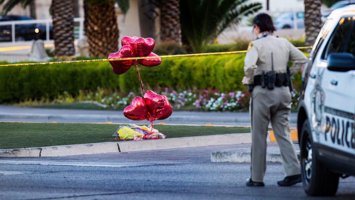 A police officer walks by heart balloons and flowers near the shooting scene in Las Vegas.