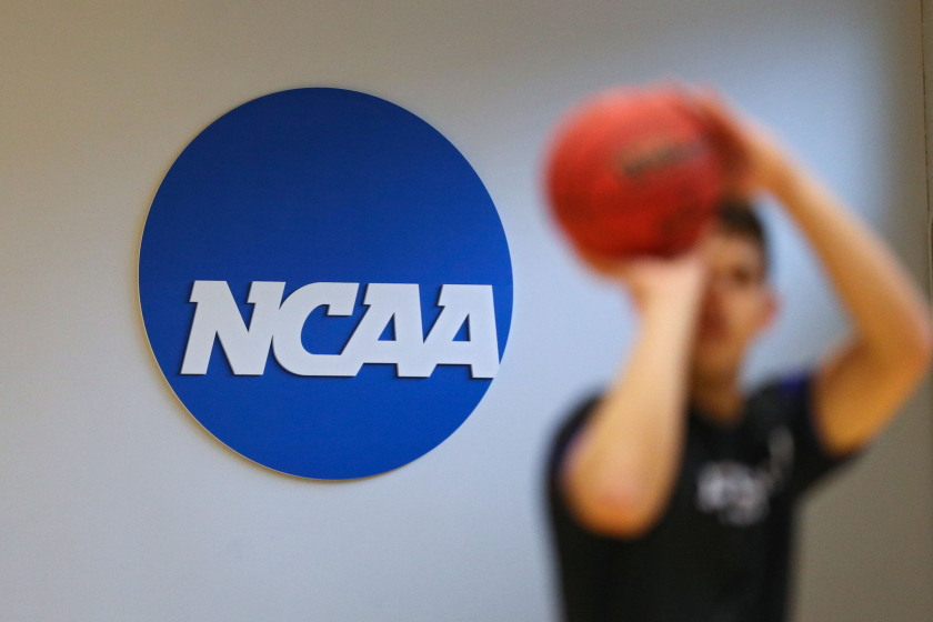 A basketball player shoots in front of the NCAA logo.