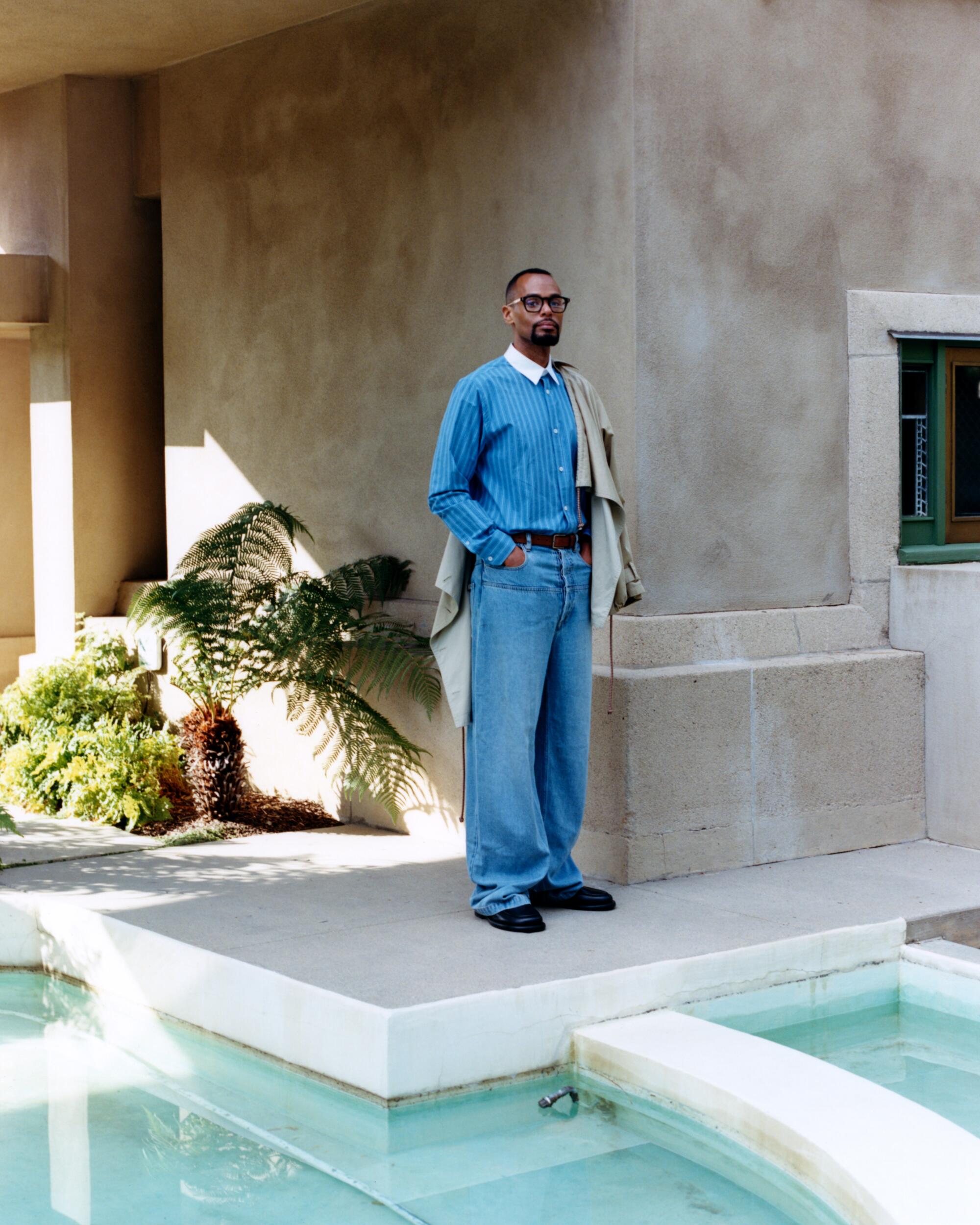 A man in an all-blue outfit stands beside a pond.